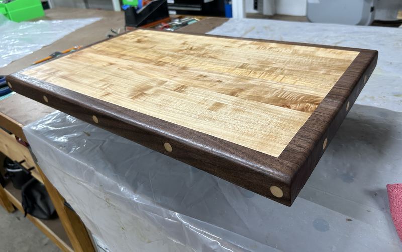 Curly maple cutting board with a walnut border and maple plugs