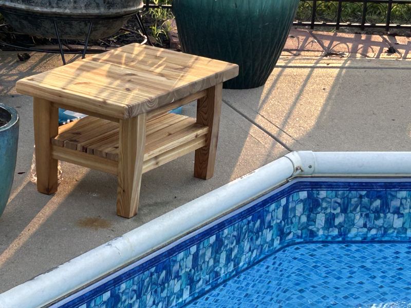 Wooden outdoor side table with slatted lower shelf beside a pool