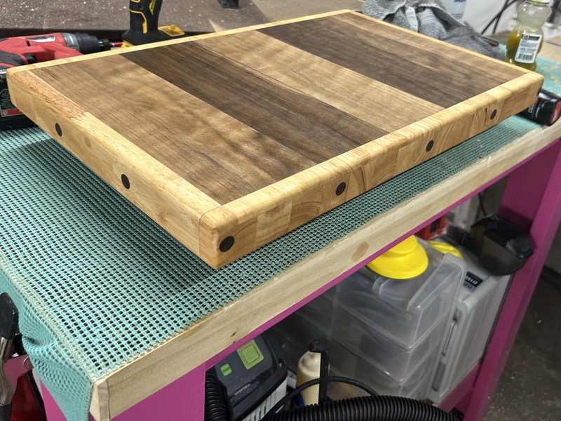 Walnut cutting board with a maple border and dark plugs, on the shop cart
